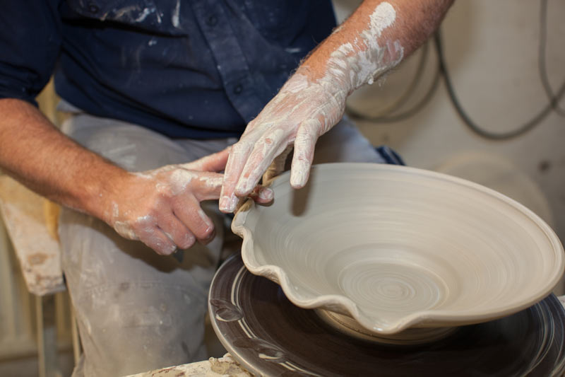 Ein keramiker bearbeitet an einer Drehscheibe den Ton